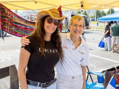 Two women at exhibitor booth under a tent smiling at camera.