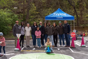 A group of people posing for a photo at an outdoor event, with a blue tent and pink cones in the background.