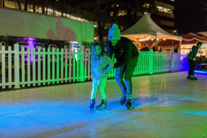 A father and daughter learning to ice skate together, with the father providing guidance and support