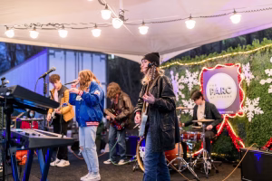 A rock band performing at an outdoor event, with the lead singer and guitarist taking center stage.