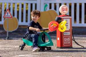 A young boy enjoying a toy car ride near a nostalgic gas station