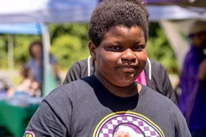 A young boy with dark skin and short, curly hair, wearing a gray t-shirt with a logo on it