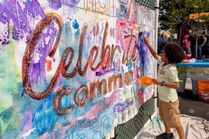 A young boy painting a mural with the words 'Celebrating Community' on it