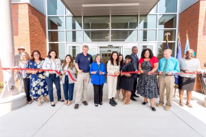 A group of people cutting a red ribbon in front of a building, symbolizing the opening of a new facility or event.