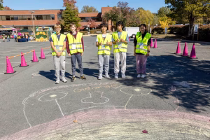 Five children in yellow vests standing in a parking lot