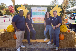 Four people posing for a photo at a fall festival with pumpkins and hay bales in the background.