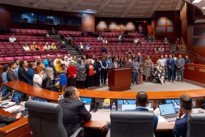 A group of people standing in a large room with rows of red seats