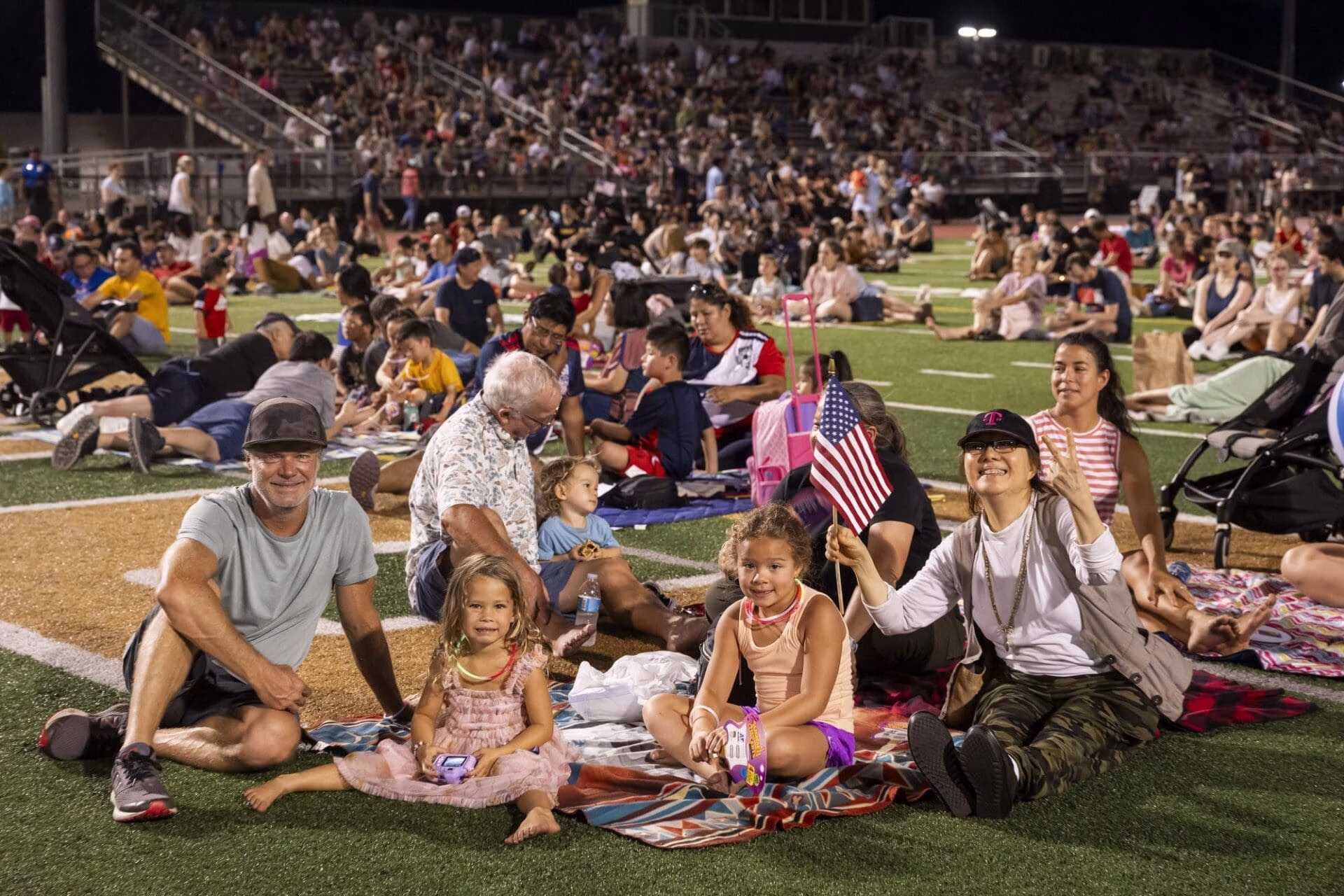 A large crowd of people sitting on a football field, enjoying the event