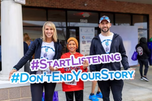 A family of three holding a sign that reads #StartListening #DontEndYourStory, standing in front of a brick building with a glass door and window