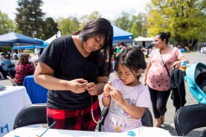 Two young girls making beaded necklaces at an outdoor event