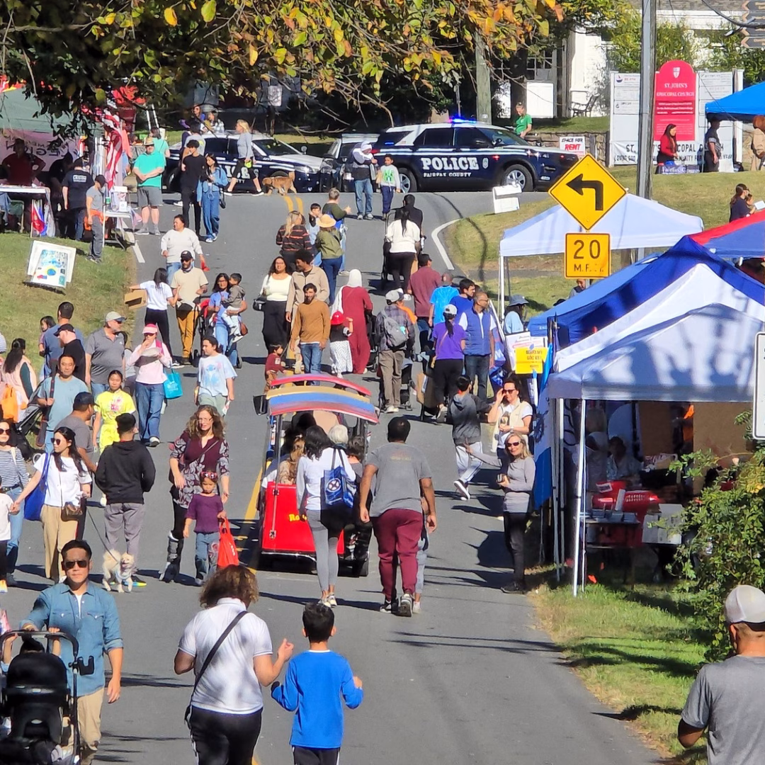 A crowd of people walking down a street at an outdoor festival.