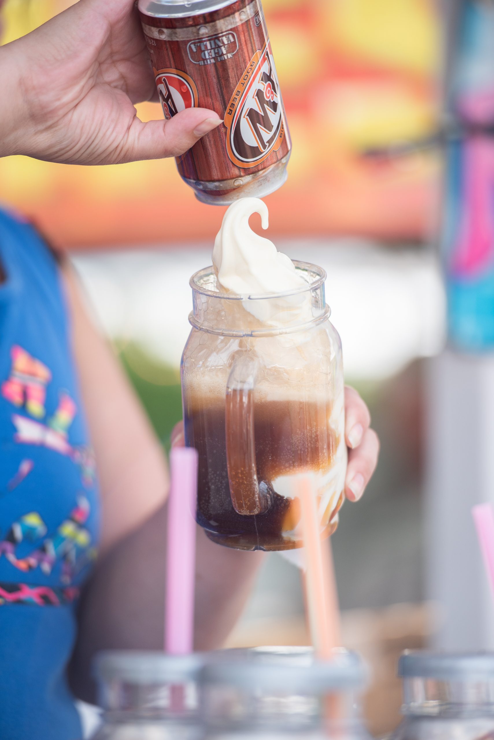 A person pouring a root beer float into a glass with a straw
