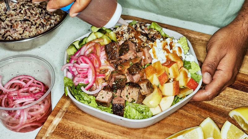 A salad with mixed greens, vegetables, fruits, and meat, topped with a savory sauce