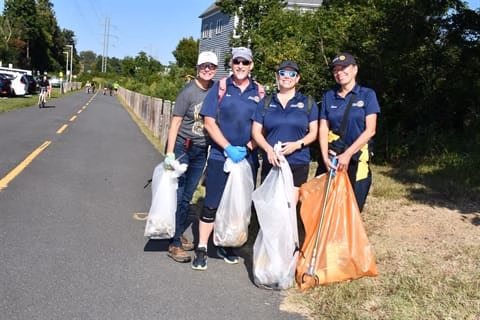 Three women in blue shirts and hats, holding trash bags and grabbers, cleaning up the road